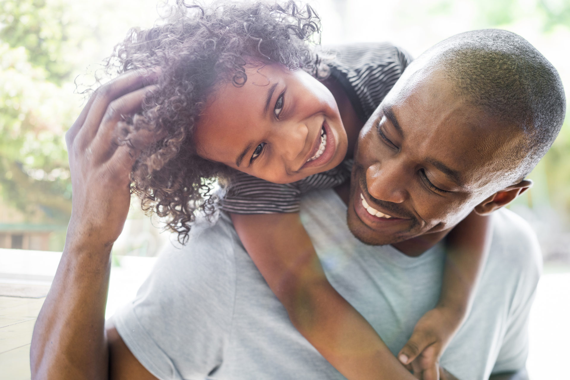 A photo of happy girl with arms around father. Young man is looking at daughter smiling. They are in casuals at home.