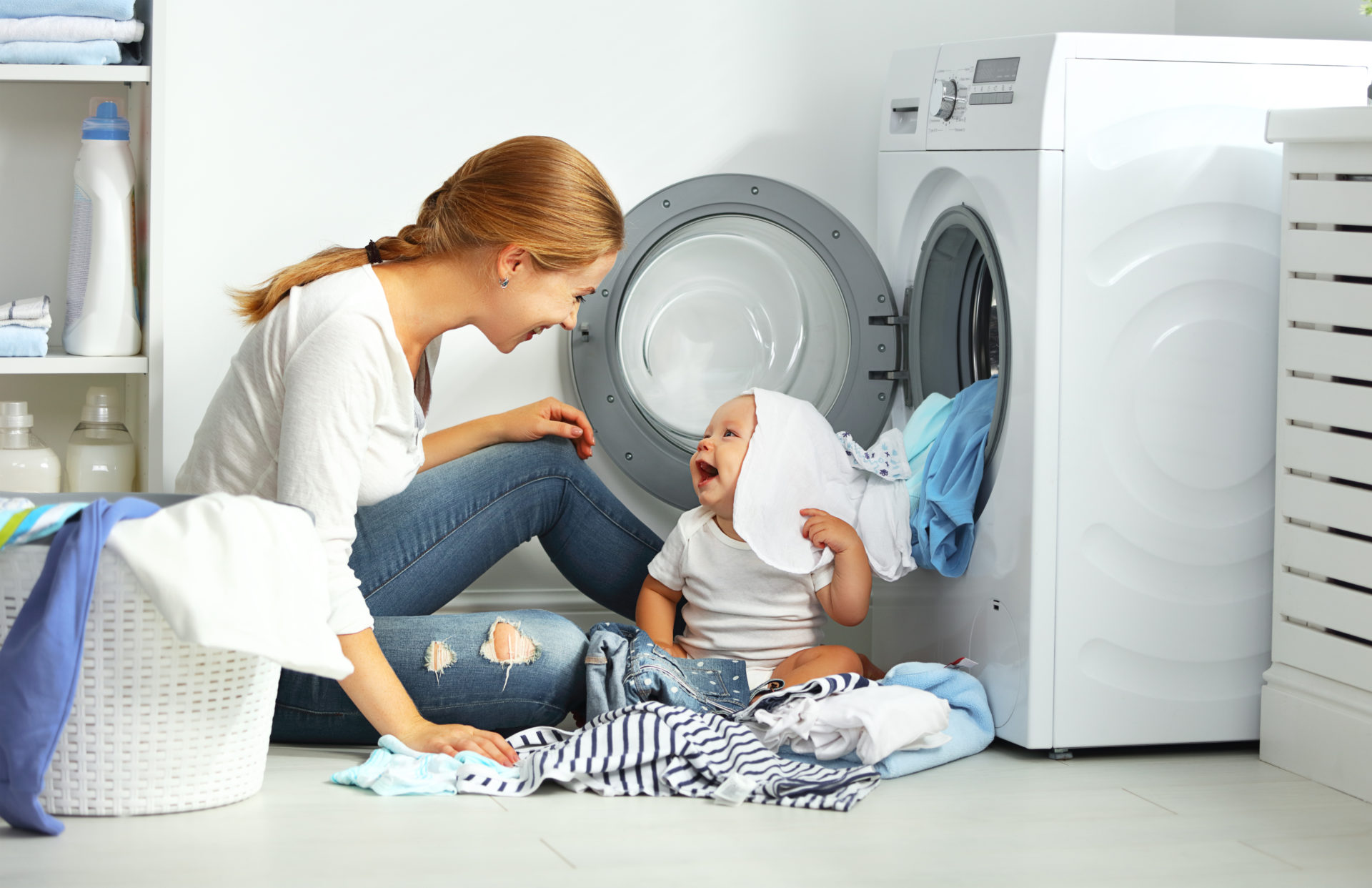 mother a housewife with a baby engaged in laundry fold clothes into the washing machine