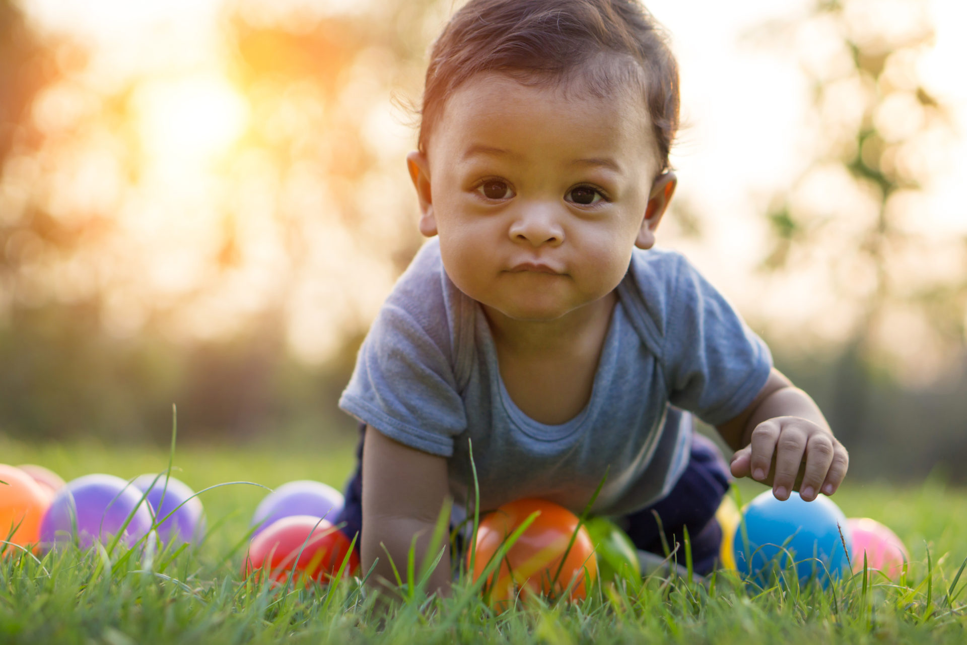 Cute asian baby crawling in the green grass and colorful ball - Sunset filter effect