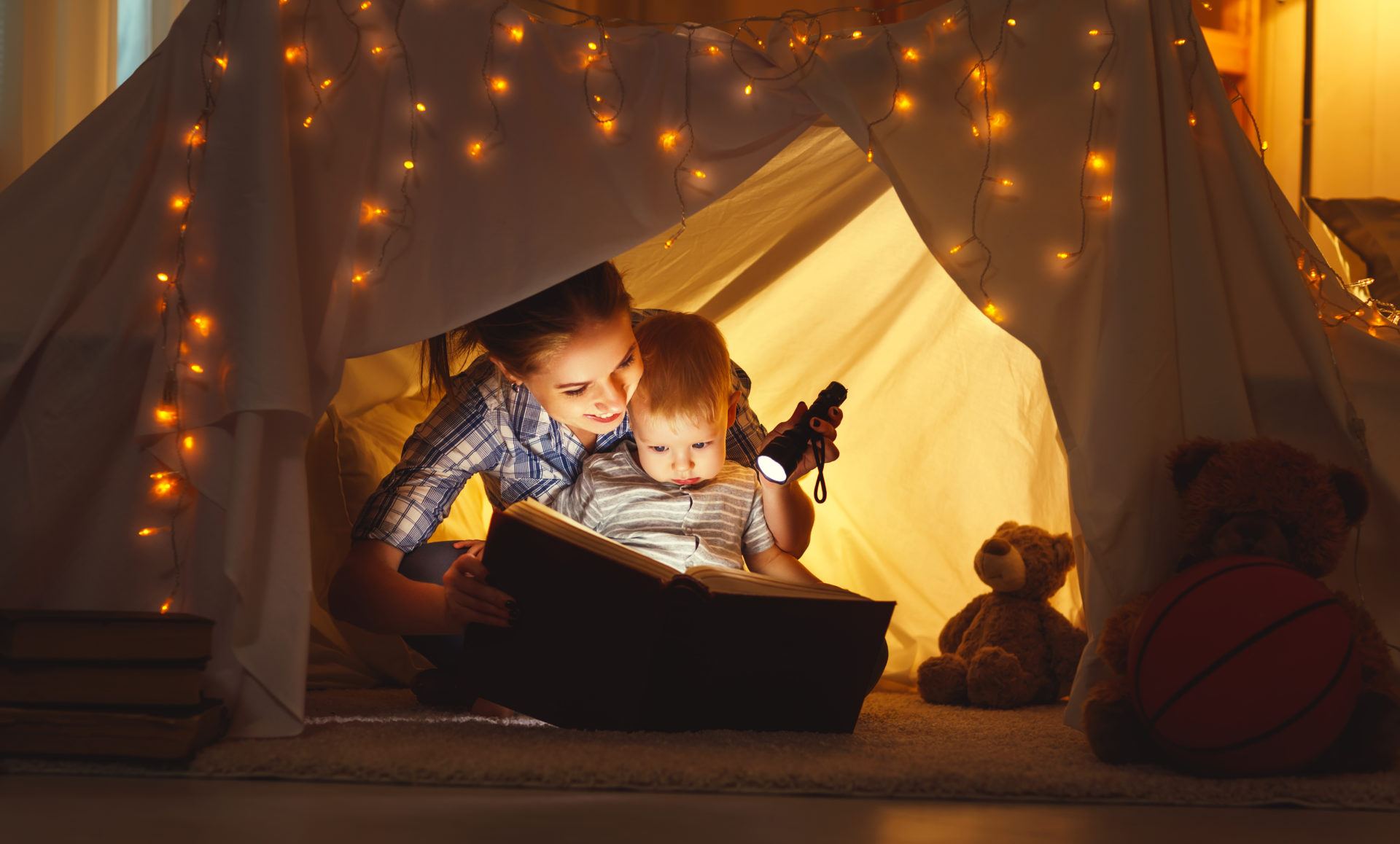 reading and family games in children's tent. mother and child daughter with  book and flashlight before going to bed