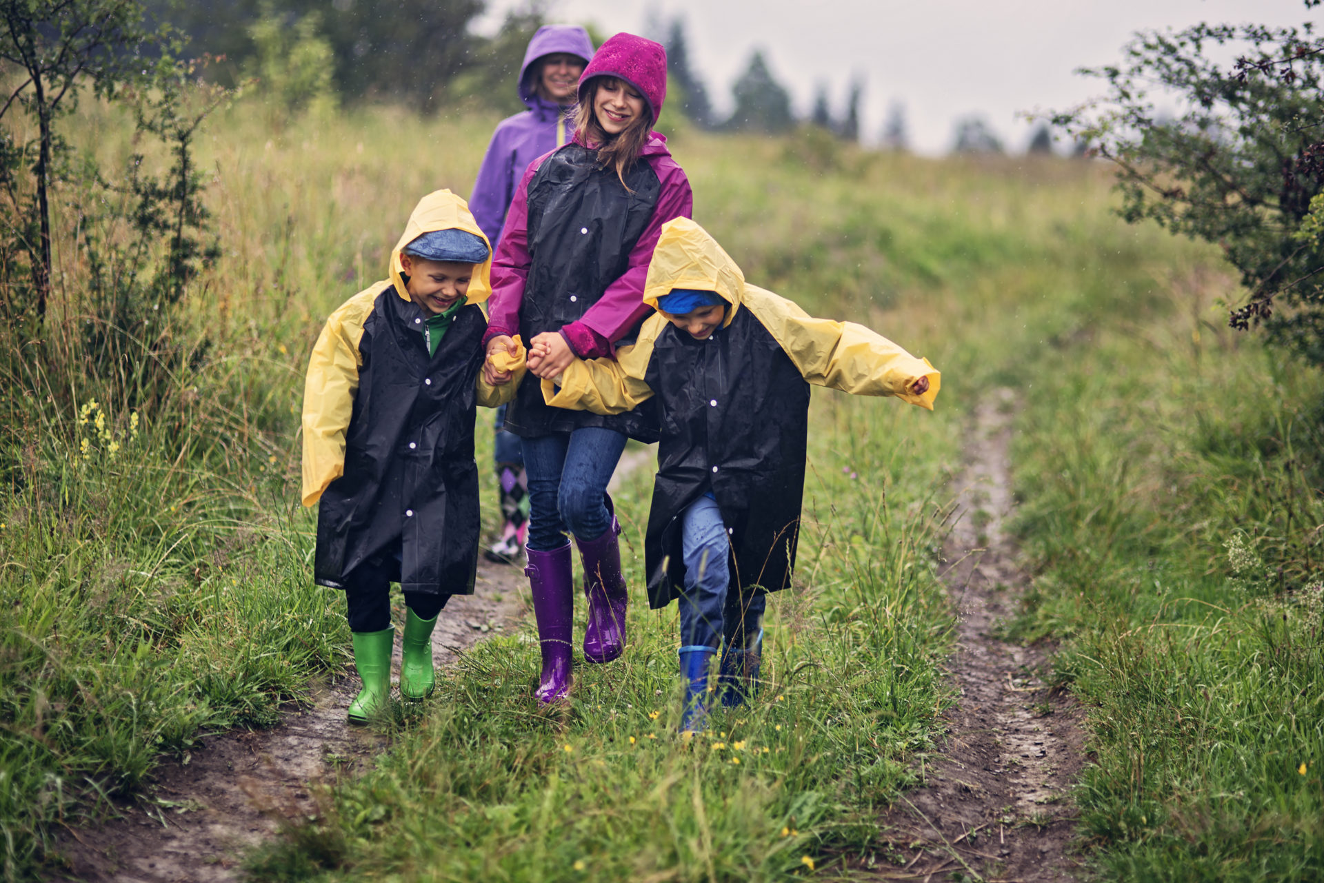 Family wearing raincoats and windproof jackets is hiking on dirt path in nature.