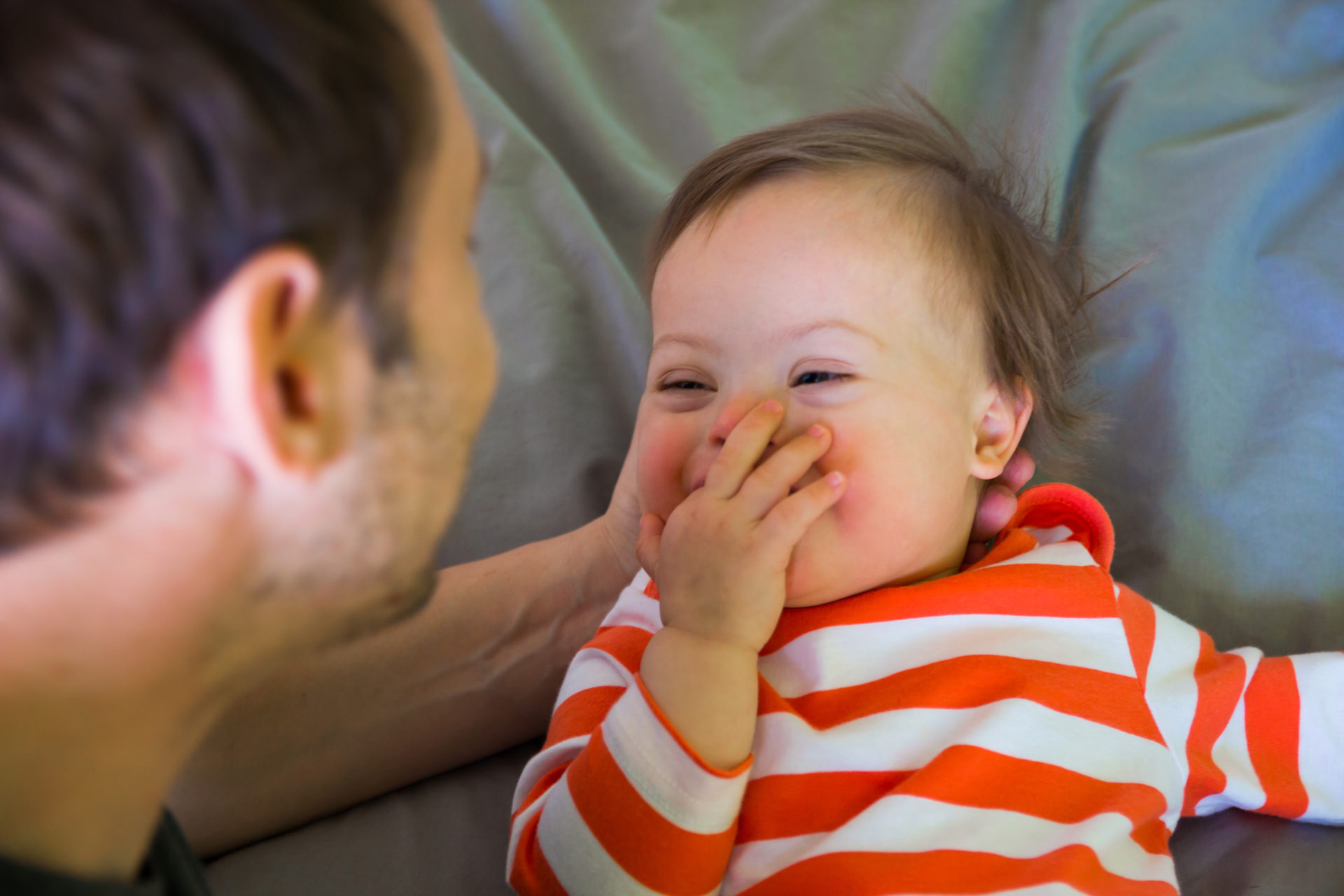 Cute baby boy with Down syndrome playing with dad on the bed in home bedroom