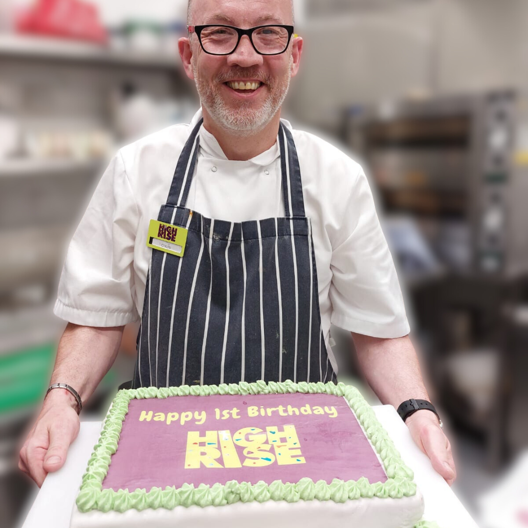 High Rise Café Hospitality Manager Colin Smiling while holding a cake for the High Rise 1st Birthday Party